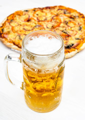 Glass with beer and baked pizza on the white table.