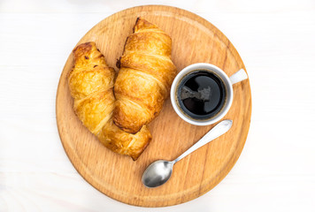 Cutting board with cup of coffee and two croissants on the white table. Top view.
