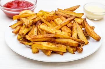 Plate with french fries and saucers with sauces on the white wooden table.