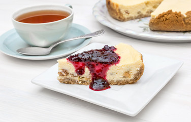 Cup of tea with piece of cheesecake with jam on the table.
