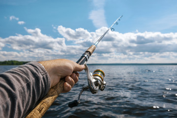 fishing rod in the hand on the background of a wide river on a s