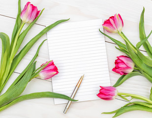 Fototapeta premium Blank notepad and bouquet with tulips on the wooden table. Top view.