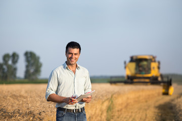 Engineer with notebook and combine harvester in field