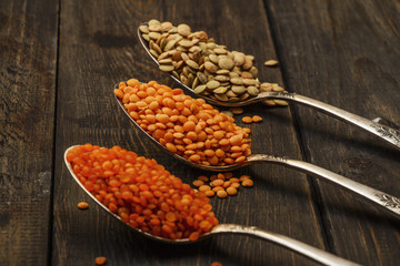 Lentil seeds on a wooden table in silver spoons. Seeds of red and green food additives of lentils. Useful lentils of the legume family.
