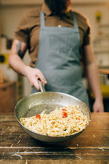 Male chef holds pan with pasta, fettuccine cooking