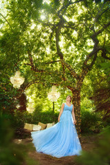 Beautiful woman in blue lush dress in fairy forest. From above hang crystal chandeliers
