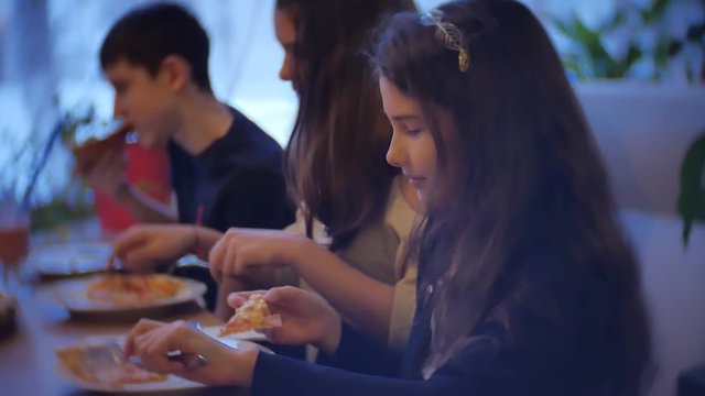 group kids family of people eat pizza at a cafe. close-up indoors children teens eating fast food in cafe slow motion video