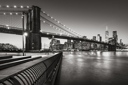 Fototapeta Brooklyn Bridge Park boardwalk in evening with the skyscrapers of Lower Manhattan, East River, and the Brooklyn Bridge in Black & White. Brooklyn, New York City