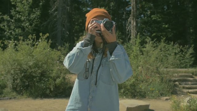 medium shot of a young Asian woman taking a picture with her vintage camera in a national forest park