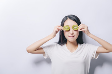 Studio portrait of young funny girl holding two orange slices on eyes on white background and biting her lips. Fresh fruits and healthy diet concept. Free copy space provided