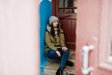 Portrait of brunette girl in gray scarf and hat, glasses against entrance.