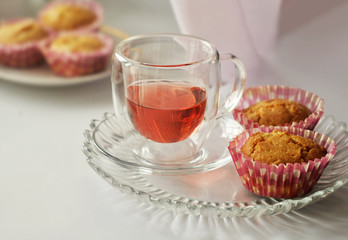 Tea in a glass cup and two homemade cupcakes are on a glass plate. Close-up