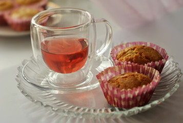 Tea in a glass cup and two homemade cupcakes are on a glass plate. Close-up