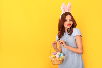 Young woman studio isolated on yellow wearing bunny ears holding basket with eggs joyful