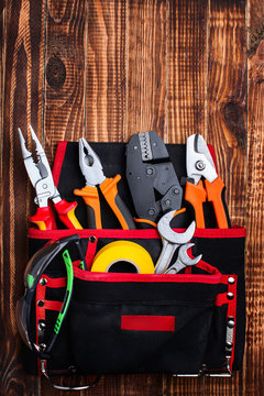 background of professional electrician tools in the pockets of the loincloth on a wooden background