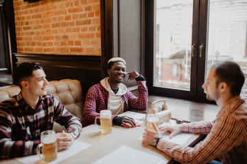 Multiracial friends talking and drinking beer and clinking glasses at pub