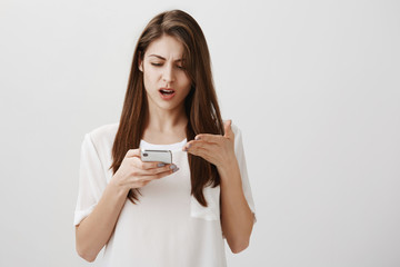 Woman received absurd message. Portrait of displeased annoyed good-looking girl holding smartphone...