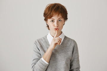 Portrait of serious worried redhead woman with short messy haircut and freckles saying shush while holding index finger near mouth, expressing confidence. Keep silent and do not spread this secret