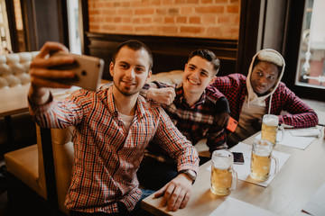 Happy male friends taking selfie and drinking beer at bar or pub