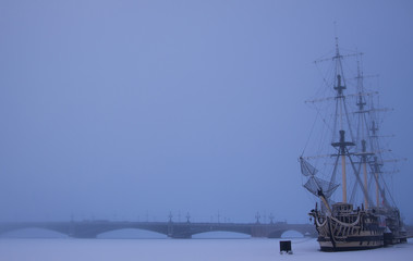 Foggy winter view of the frigate nearby Petrovskaya embankment and frozen Neva river covered with snow and the Trinity Bridge background. St. Petersburg, Russia.