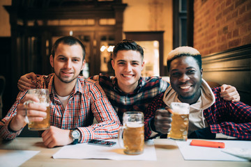 Multiracial friends group drinking and toasting beer at pub. Friendship concept with young people enjoying time together and having fun.