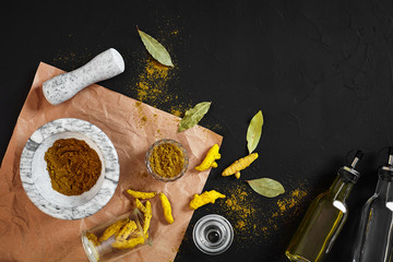 Turmeric Haldi powder in small bowl with raw whole in marble mortar over black background with copy space
