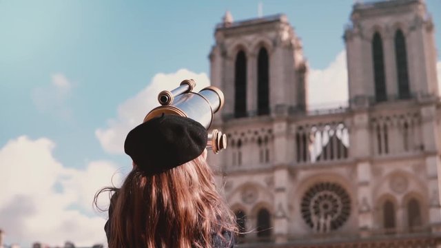 Girl child in beret looks through coin binocular. Slow motion. Notre-Dame de Paris. Female kid using view telescope.