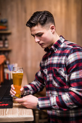 Young man with beer bottle using phone at counter in pub