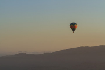 A single hot air balloon over the rolling hills and vineyard of Napa Valley, California, at sunrise