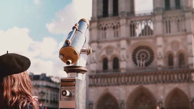 Little girl in beret using coin-operated telescope. Slow motion. Notre Dame de Paris. Stationary binoculars. Vacation.