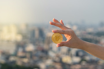 Closeup hand holding bitcoin over the cityscape blurred background, business and cryptocurrency concept