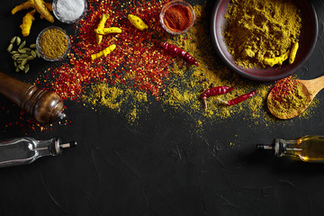 Cooking using fresh ground spices with big and small bowls of spice on a black table with powder spillage on its surface, overhead view with copyspace