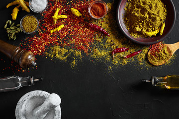 Obraz na płótnie Canvas Cooking using fresh ground spices with mortar and small bowls of spice on a black table with powder spillage on its surface, overhead view with copyspace