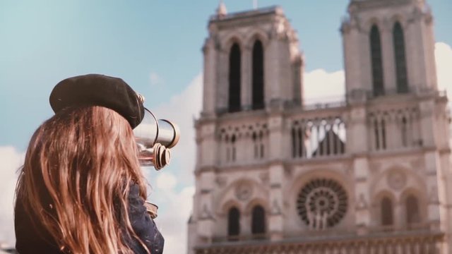 Girl child in beret looks through coin binoculars. Slow motion. Notre-Dame de Paris. Coin-operated telescope. Tourism.