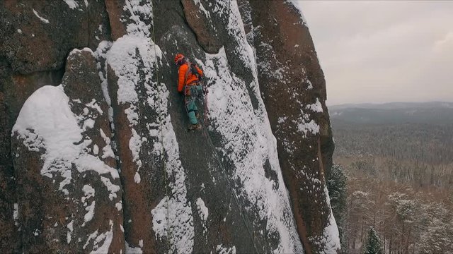 Aerial view of a rock climber climbing a steep cliffs during a sunny winter day.