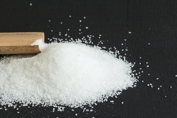 Salt on black background with wooden scoop close up