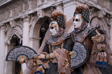 Obraz premium Two women in ornate costumes and painted masks, standing in St Marks Square during Venice Carnival (Carnivale di Venezia)