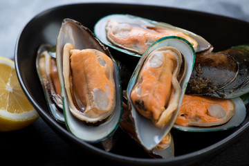 Black bowl with raw kiwi mussels, close-up, selective focus, horizontal shot