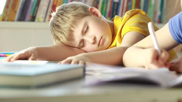 Tired schoolboy sleeping in classroom at school.
Elementary school student sleeping at classroom.