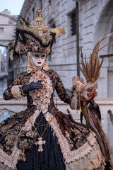 Fototapeta na wymiar Woman in costume and mask, carrying feathered bird and birdcage, photographed during the Venice Carnival (Carnivale di Venezia)
