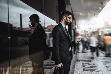 Handsome young caucasian bearded man employer in a formal suit is standing next to a bus stop and...