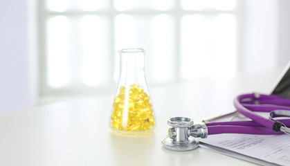 closeup of the desk of a doctors office with a stethoscope in the foreground and a bottle with pills in the background