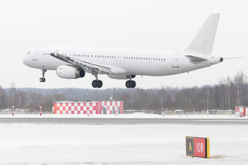 Modern passenger airplane landing at airport in winter time. Low over the runway. Transportation, aviation concept