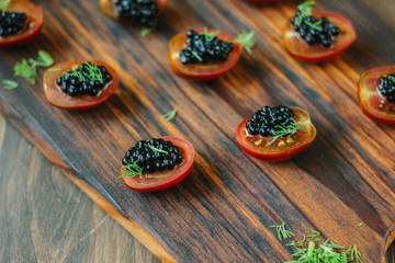 Red cherry tomatoes and black caviar appetizers on wooden board.