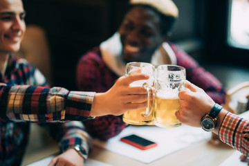 Happy multiracial smiling male friends clinking with beer mugs in pub