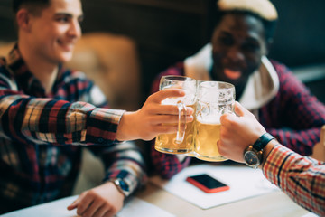 Cheers, my friends. Three handsome men are cheers mug, drinking beer, celebrating meeting and smiling.