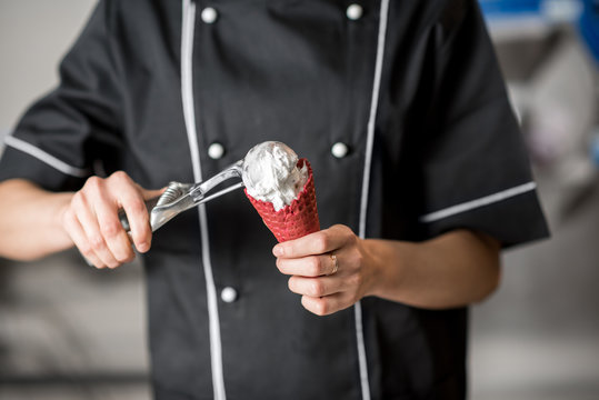 Chef cook filling with white ice cream a red waffle cone indoors. Cropped image with no face focused on hands