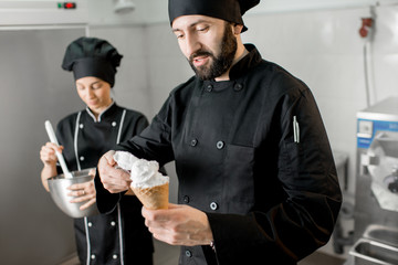 Chef cook filling ice cream into the waffle cone standing with woman assistant in the small manufacturing