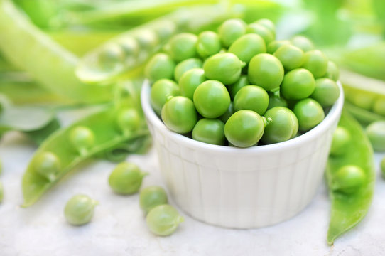 Bowl of fresh harvested green peas on pods background, selective focus