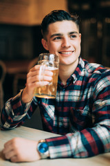 Young man sitting at pub table with a pint of light beer